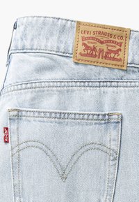 Jean en denim bleu clair avec une étiquette en cuir portant la mention "Levi Strauss & Co." au niveau de la taille et une couture en forme de V distinctive sur la poche arrière.
