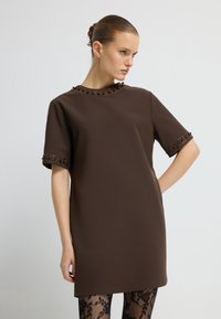 Brązowa sukienka o krótkim rękawie z okrągłym dekoltem, ozdobiona koralikami przy kołnierzyku i brzegach rękawów, wykonana z gładkiego materiału.