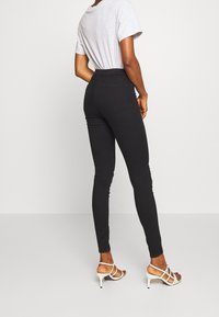Jeans skinny negros con cintura alta y bolsillos traseros, combinados con una camiseta gris clara y tacones blancos con tiras. Textura de tejido suave.