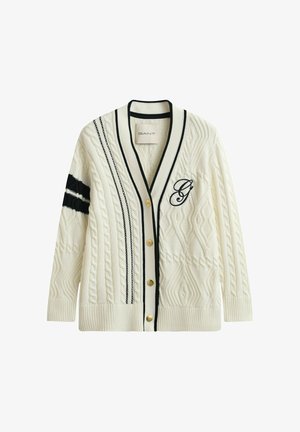 Cárdigan de punto grueso color crema con rayas negras, botones dorados y una "G" bordada en el pecho, que presenta un escote en V profundo y puños y bajo acanalados.