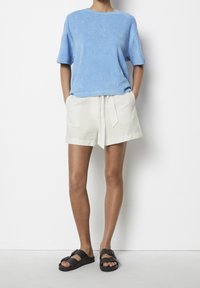 Ljusblå, kortärmad frottétröja; gräddvita, höga linne-shorts med knytbälte; svarta, platta sandaler med två spännen.