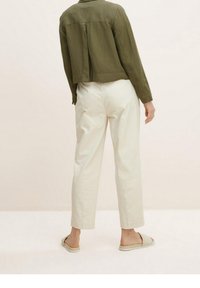 Camicia cropped verde oliva, pantaloni bianchi a gamba dritta e sandali slip-on casual. Tessuto leggero con una vestibilità rilassata e una sottile trama.