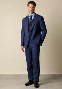 Marineblauwe kostuum met een getailleerde pasvorm, voorzien van een bijpassend vest en een gestreept overhemd. Zwarte leren schoenen maken de formele look compleet. Glad stofoppervlak.