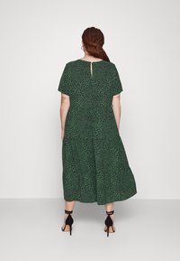 Grünes, blütenmusterndes Midikleid mit kurzen Ärmeln, Schlüssellochdetail auf der Rückseite und einer fließenden Form, kombiniert mit schwarzen High-Heels.