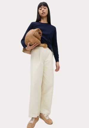 Navy knitted long-sleeve top, cream wide-leg trousers, brown quilted bag with a twisted handle, and beige sneakers with white laces.