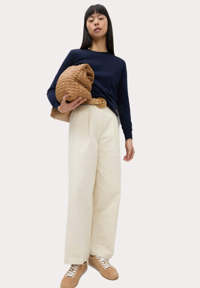 Haut en tricot à manches longues bleu marine, pantalon large crème, sac matelassé marron avec une poignée torsadée, et baskets beiges avec des lacets blancs.