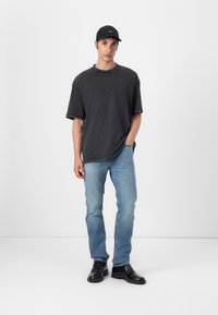 Black oversized t-shirt, light blue jeans, and black leather boots on a model. The shirt has a subtle logo and raw edges.