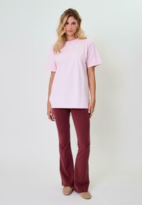 Světle růžové oversized tričko s krátkými rukávy, ve spojení s bordovými rozšiřujícími se kalhotami. Outfit má volný střih a jemnou texturu látky.