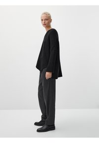 Czarny, oversize sweter o teksturowanej tkaninie i szerokich rękawach, zestawiony z ciemnymi spodniami w prążki i skórzanymi botkami za kostkę.