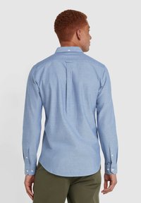 Camicia a maniche lunghe azzurro chiaro con colletto button-down, dettagli con plissettature posteriori e bottoni ai polsini, realizzata in tessuto testurizzato.
