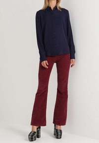 Navy button-up shirt, red corduroy flared pants, black and white patterned platform shoes. Smooth fabric, tailored fit, and high waist.