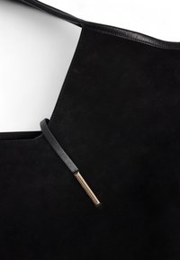 Melna zamša iepirkumu soma ar plašu atvēršanu, aprīkota ar platu melnu ādas siksnu un zelta toņa akcentu siksnas stiprinājumā.