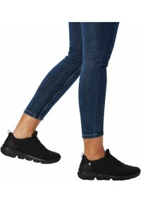 Baskets de sport noires avec une tige en mesh respirant, un bout arrondi et une semelle rembourrée. Portées avec un jean skinny bleu foncé, mettant en avant la zone des chevilles.