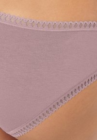 Lyse lilla undertøj med en glat tekstur, dekoreret med delikat bølget kant langs linningen. Simpelt design uden mønstre.