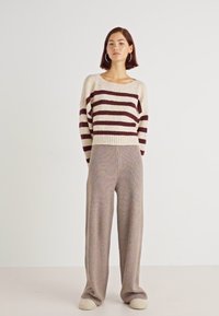 Gestreepte trui in een crème en bordeaux-wolmix, gecombineerd met brede ribgebreide beige broeken. Horizontale strepen; relaxte pasvorm.