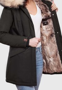 Grüne Parka mit einer Kapuze aus Kunstpelz. Verfügt über einen Reißverschluss vorne, Druckknopf-Taschen und ein weiches, plüschiges Innenfutter. Gestickte Details sind sichtbar.
