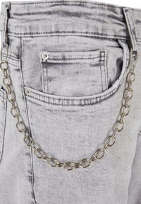 Hallide denim püksid, mille tagatasku on kinnitatud hõbedase ahelaga, millel on ovaalsed lingid ja tekstureeritud pind, luues kontrastse detaili.