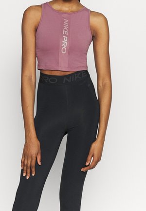 Kobieta ubrana w fioletowy bezrękawnik Nike Pro oraz czarne legginsy Nike Pro z wysokim stanem, stojąca na tle jednolitego białego tła.