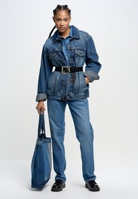 Jeansjacke mit tailliertem Schnitt, hellblauem Hemd und passender Jeans. Schwarze Tasche, glatte Textur, klassischer Schnitt und Knopfakzente.