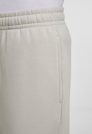 Bežid värvusega dressipüksid, millel on elastne vöökoht ja küljetasku, kantud valge soonikkoes toppiga.