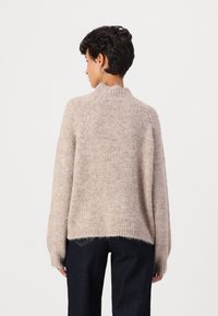 Light beige knitted sweater with a high neck, relaxed fit, long sleeves, and ribbed hem, paired with dark denim jeans.