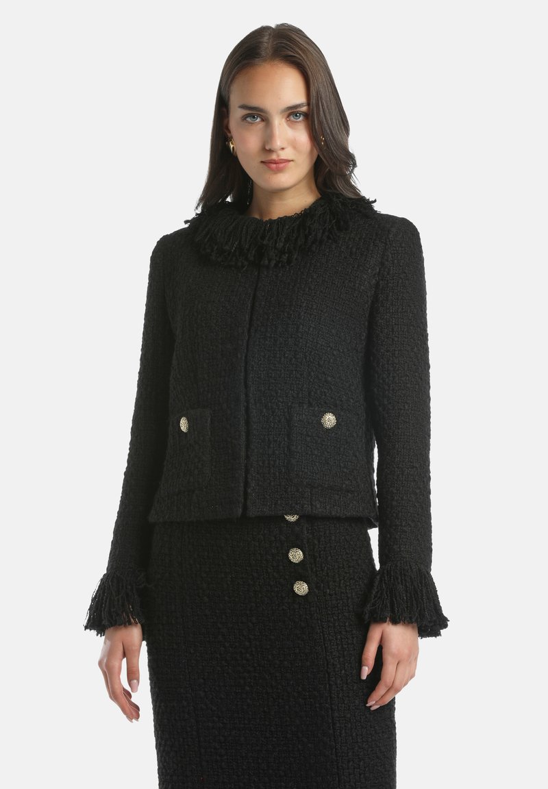 Giacca nera con texture, caratterizzata da un colletto frangiato, due tasche frontali e bottoni decorativi. Le maniche presentano accenti arricciati ai polsini.