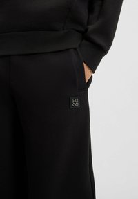 Schwarzes Sweatshirt- und Hosen-Set mit weicher Textur. Mit einer Tasche und einem schwarzen Gummilogo-Patch an der Hose. Klassische Passform.