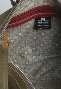 L'interno della borsa di pelle verde presenta un motivo geometrico a stella in marrone e blu chiaro, con una cerniera rossa e l'etichetta del marchio visibile.