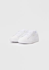 Ein Paar weiße, niedrige Puma-Sneaker mit weißen Schnürsenkeln und subtil goldenem Puma-Logo an der Seite vor einem weißen Hintergrund.