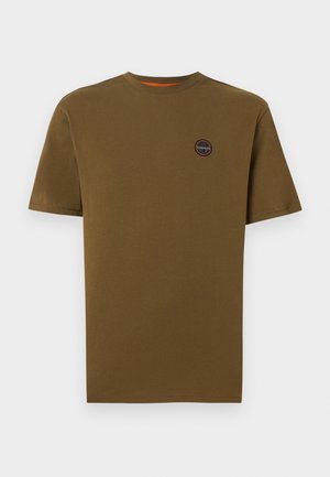 Ruskea lyhythihainen pyöreäkauluksinen t-paita, jossa pieni pyöreä logoplässi vasemmalla rinnalla, yksiväristä taustaa vasten.