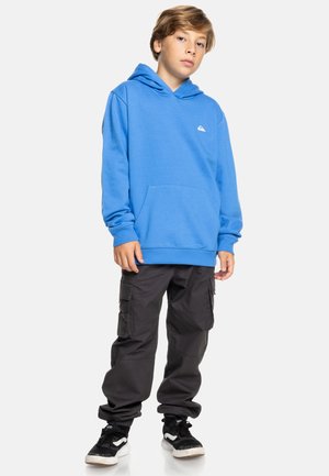 Sudadera de algodón azul con un bolsillo canguro y capucha con cordón. Combinada con pantalones cargo negros que tienen bolsillos laterales y puños elásticos.