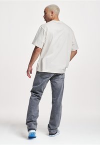 Short-sleeve cream t-shirt with a relaxed fit, paired with gray jeans. The outfit features textured fabrics and light blue sneakers.