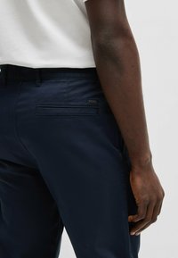 Marineblauwe broek van zachte stof met voor- en achterzakken, voorzien van een subtiele logotag aan de achterkant. Aansluitende silhouet met een casual ontwerp.