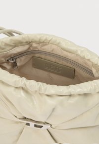 Μπεζ δερμάτινη τσάντα χειρός με μαζεμένο επάνω μέρος, ασημένια πόρπη και εσωτερική επένδυση από ύφασμα μπεζ που δείχνει μια τσέπη με φερμουάρ και το λογότυπο της Diesel.