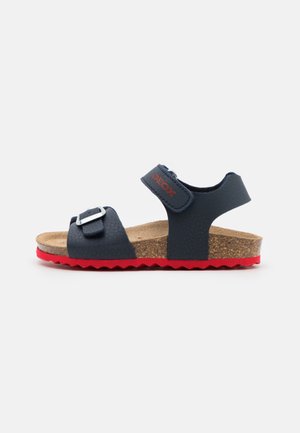 Børnesandal i marineblå med korksål, justerbar frontspænde, bagrem og rød tekstureret sål.