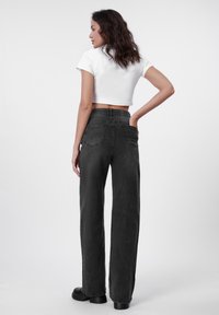 Svart vid benjeans med høy midje, med to baklommer, en teksturert fabric, og et glatt, rent design. Kombinert med en hvit kort topp.