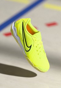 Scarpa sportiva gialla neon con tomaia in rete texturizzata, intersuola bianca, accento del logo nero e suola in gomma.