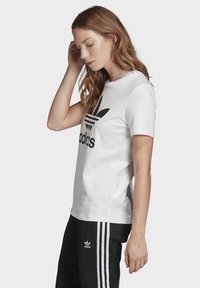 Witte katoenen T-shirt met korte mouwen met een groot zwart Adidas-logo en drie horizontale strepen. Gedeelte textuur, eenvoudig ontwerp.