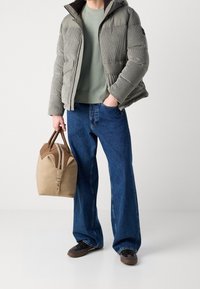 Kurtka puchowa z jasnoszarego sztruksu, zielony sweter o okrągłym dekolcie, niebieskie jeansy o szerokich nogawkach oraz beżowa skórzana torba z brązowymi akcentami. Brązowe buty.