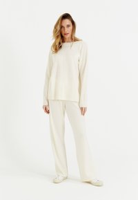 Maglione di colore crema a maglia con maniche lunghe e taglio dritto, abbinato a pantaloni a gamba larga coordinati, entrambi in un tessuto morbido e texturizzato.