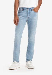 Light blue denim jeans with a straight cut, featuring a classic five-pocket design and a button fly. Paired with white sneakers.