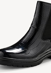 Botte Chelsea noire avec une texture crocodile brillante, des panneaux latéraux élastiques et une semelle en caoutchouc épaisse pour la durabilité et l'adhérence.