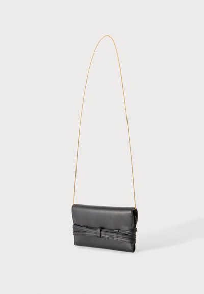 Μαύρο δερμάτινο clutch με λεπτό χρυσό λουράκι ώμου και διακοσμητική ραμμένη λεπτομέρεια στο μπροστινό λουράκι, εμφανίζεται σε απλό ανοιχτό φόντο.