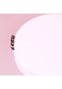 Black false eyelashes feature a soft, curled design, displayed against a round white surface with a light pink background.