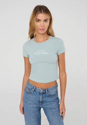 T-shirt corto azzurro chiaro con scollo rotondo e maniche corte, caratterizzato da un design testuale bianco "Côte d'Azur Saint-Tropez Tennis Club".