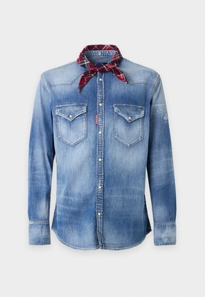 Homme portant une chemise en jean délavée, un jean déchiré, des bottes noires, une casquette noire, un foulard rouge à carreaux autour du cou et une ceinture noire avec une boucle en forme de feuille d'érable rouge.