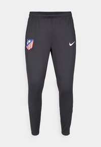 Pantalons de sport noirs en tissu extensible, présentant un logo de l'Atlético de Madrid sur le côté gauche et un swoosh blanc de Nike sur le côté droit.