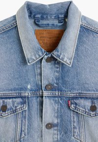 Jasnoniebieska kurtka dżinsowa z wyłużonym kołnierzem, miedzianymi stugami i dwoma kieszeniami na piersi z zapięciami na guziki. Widoczna metka marki.