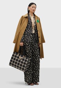 Hnedý trenčkot cez čiernu blúzku s bodkami a zodpovedajúce široké nohavice. Kabelka s čierno-bielym vzorom a zlatými kovovými prvkami.