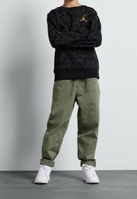 Felpa nera con motivo a rilievo del logo, colletto girocollo e orlo a contrasto. Pantaloni larghi verde oliva e sneaker bianche completano il look.